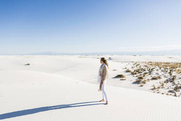 A teenage girl standing looking at a vast open space of sand dunes. - MINF14321