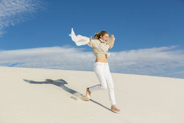 A teenage girl leaping and dancing in light white sand in a dunes landscape. - MINF14326