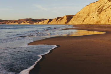 Beach at dawn, with sheer cliffs and rocks. - MINF14372