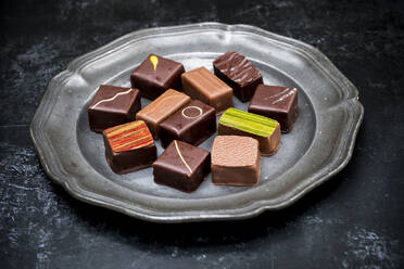 Nahaufnahme einer Auswahl von Schokoladenpralinen auf einem Zinnteller vor schwarzem Hintergrund. - MINF14448