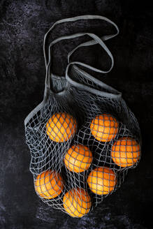 Nahaufnahme von Orangen in einem grauen Netzbeutel auf schwarzem Hintergrund. - MINF14449