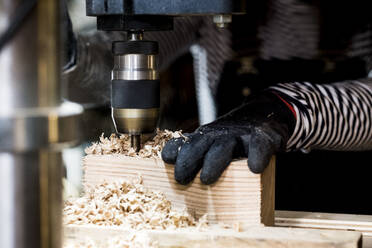 Close up of person wearing protective gloves using electric drill in wood workshop. - MINF14470