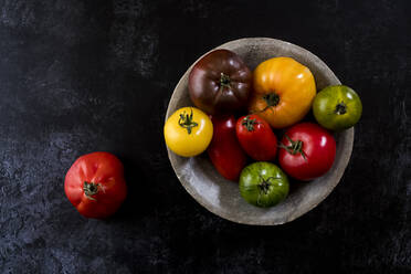 High angle close up of grey plate with selection of tomatoes in various shapes and colours on black background. - MINF14487