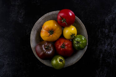 High angle close up of grey plate with selection of tomatoes in various shapes and colours on black background. - MINF14488