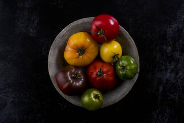 Nahaufnahme eines grauen Tellers mit einer Auswahl von Tomaten in verschiedenen Formen und Farben auf schwarzem Hintergrund. - MINF14488