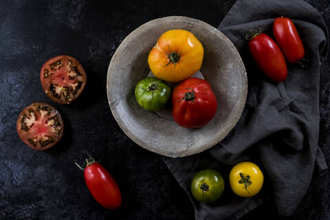 Nahaufnahme eines grauen Tellers und eines Tuchs sowie einer Auswahl frischer Tomaten auf schwarzem Hintergrund., lizenzfreies Stockfoto