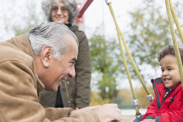 Großvater spielt mit seinem Enkel auf einer Schaukel auf dem Spielplatz - CAIF24523