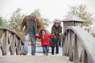 Grandparents walking with grandson on footbridge - CAIF24524