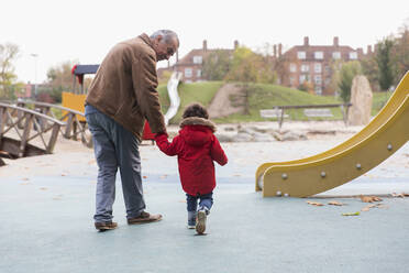 Großvater geht mit Kleinkind-Enkel auf dem Spielplatz spazieren - CAIF24534