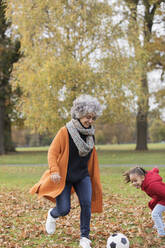 Verspielte Großmutter spielt Fußball mit Enkelin im Herbst Park - CAIF24544
