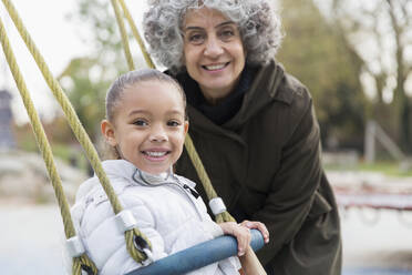 Portrait smiling grandmother and granddaughter playing on swing at playground - CAIF24549