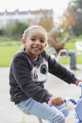 Porträt lächelndes Mädchen fährt Fahrrad auf dem Spielplatz - CAIF24551