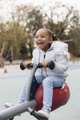 Playful, happy girl playing on playground seesaw - CAIF24560