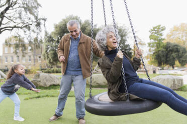 Verspielte Großeltern und Enkelin spielen auf einer Schaukel im Park - CAIF24562