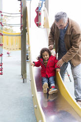 Großvater spielt mit Kleinkind Enkel auf Spielplatz Rutsche - CAIF24563