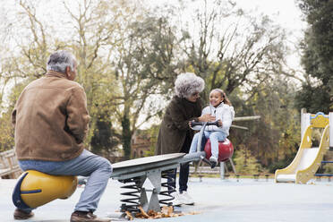 Großeltern spielen mit Enkelin auf dem Spielplatz auf der Wippe - CAIF24564