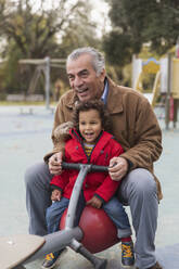 Grandfather playing with grandson on playground seesaw - CAIF24569