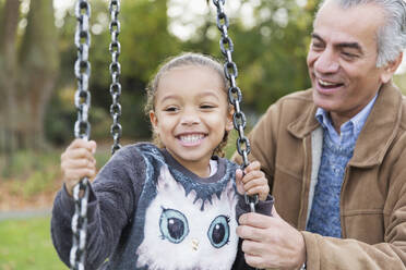 Playful grandfather and granddaughter on playground swing - CAIF24574