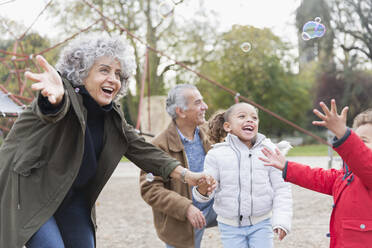 Verspielte Großeltern und Enkelkinder spielen mit Seifenblasen im Park - CAIF24576