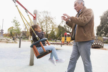 Großvater schiebt Enkelin auf Spielplatzschaukel - CAIF24582