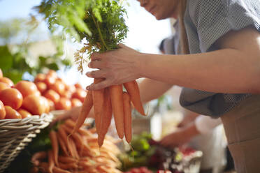 Woman holding bunch of carrots at farmer’s market - CAIF24606