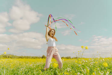 Glückliche junge Frau, die sich mit bunten Bändern auf einer Blumenwiese im Frühling bewegt - ERRF02886