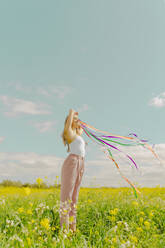 Junge Frau mit bunten Bändern auf einer Blumenwiese im Frühling - ERRF02888