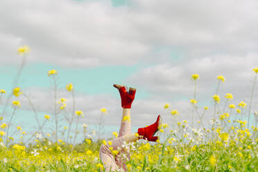 Beine einer Frau in roten Stiefeletten auf einer Blumenwiese im Frühling - ERRF02895