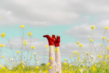 Beine einer Frau in roten Stiefeletten auf einer Blumenwiese im Frühling - ERRF02896