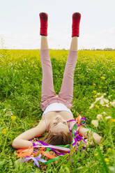 Young woman wearing red ankle boots lying in a flower meadow in spring - ERRF02898