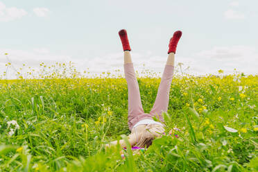 Young woman wearing red ankle boots lying in a flower meadow in spring - ERRF02899