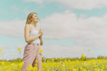 Junge Frau steht im Frühling auf einer Wiese und hält eine Blume - ERRF02904