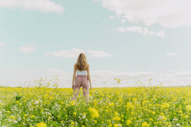 Rückansicht einer jungen Frau auf einer Blumenwiese im Frühling - ERRF02907