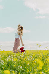 Glückliche junge Frau, die im Frühling auf einer Blumenwiese springt - ERRF02911