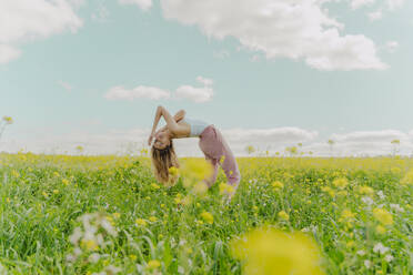 Junge Frau, die sich auf einer Blumenwiese im Frühling nach hinten beugt - ERRF02917