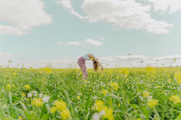Junge Frau bückt sich auf einer Blumenwiese im Frühling - ERRF02919