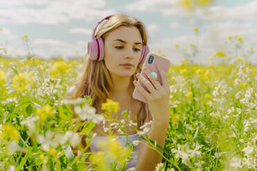 Junge Frau mit Kopfhörern und Smartphone auf einer Blumenwiese im Frühling - ERRF02928