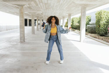 Portrait of happy young woman dancing while listening music with earphones and smartphone - TCEF00327