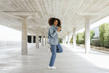 Young woman dancing while listening music with earphones and smartphone - TCEF00328