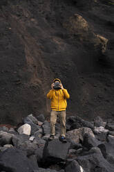 Mann steht inmitten von Vulkangestein, das sein Gesicht bedeckt, Insel Sao Miguel, Azoren, Portugal - AFVF05832