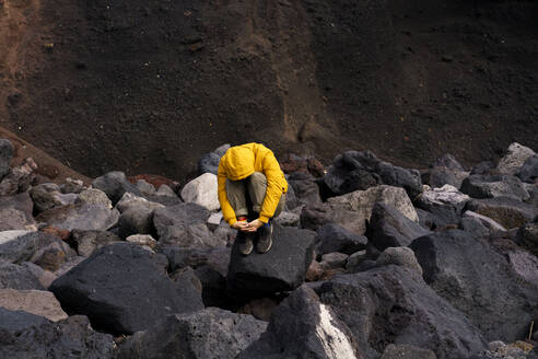 Man crouching amidst volcanic rocks, Sao Miguel Island, Azores, Portugal - AFVF05833