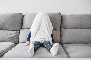 Kleines Mädchen sitzt zu Hause auf der Couch und versteckt sich unter der Bettdecke - JRFF04249