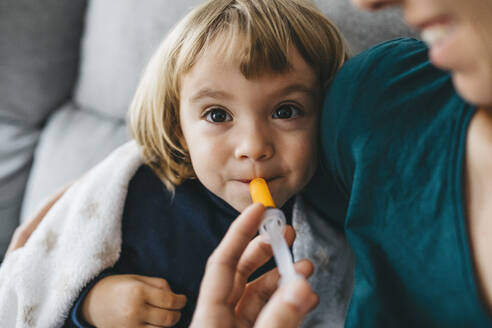 Portrait of sick little girl sitting on couch while mother giving her medication - JRFF04254