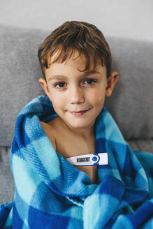 Porträt eines kranken Jungen, der mit einem digitalen Thermometer auf der Couch sitzt - JRFF04262