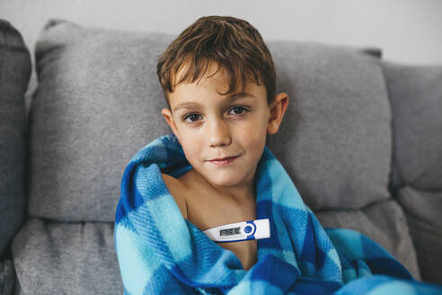 Porträt eines kranken Jungen, der mit einem digitalen Thermometer auf der Couch sitzt - JRFF04263