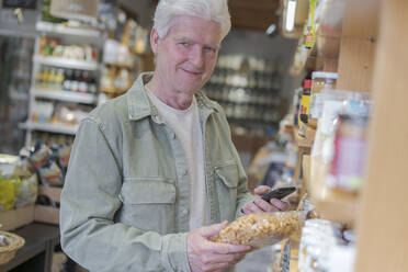 Porträt eines älteren Mannes, der in einem kleinen Lebensmittelgeschäft Lebensmittel einkauft - AFVF05847