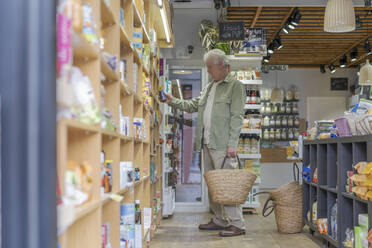 Senior man buying groceries in a small food store - AFVF05855