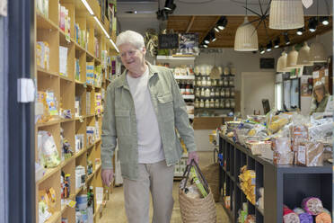 Lächelnder älterer Mann, der in einem kleinen Lebensmittelgeschäft Lebensmittel einkauft - AFVF05856