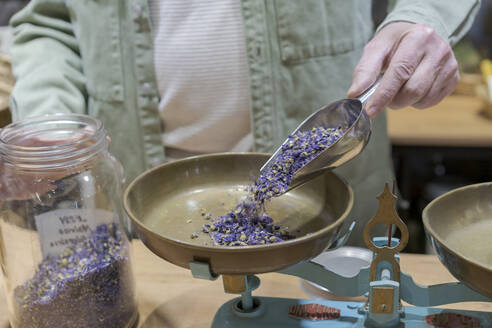 Nahaufnahme eines älteren Mannes, der in seinem Geschäft getrocknete Lavendelblüten in eine Waage gießt - AFVF05860