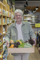 Porträt eines älteren Mannes, der eine Kiste mit Gemüse in einem kleinen Lebensmittelgeschäft trägt - AFVF05881